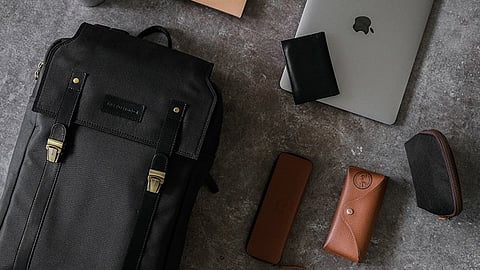 A flatlay of backpack with Apple laptop, rayban glasses and other items.