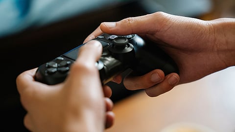 Close-up of hands holding a wireless gaming controller while playing a video game indoors.
