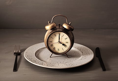 concept of intermittent fasting, ketogenic diet, weight loss. fork and knife on a plate and alarmclock