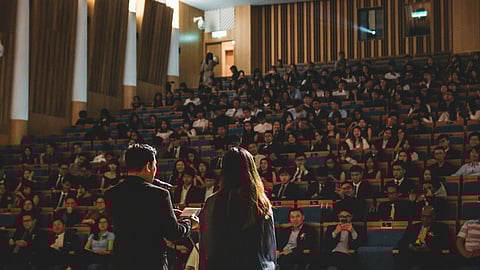A man and woman stand confidently before a large audience.