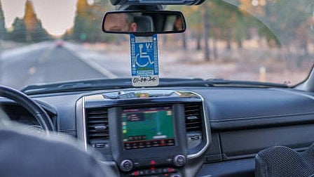 Image showing interior of a vehicle with a disability sign hanging on the rear-view mirror. 