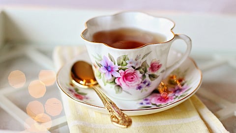 A delicate tea cup and saucer set, featuring a floral design, filled with steaming tea on a wooden table.