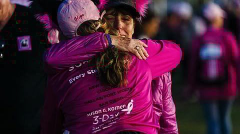 Women in pink shirts hugging each other among a crowd.