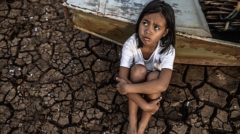 A girl sitting on a drought affected area looking up.