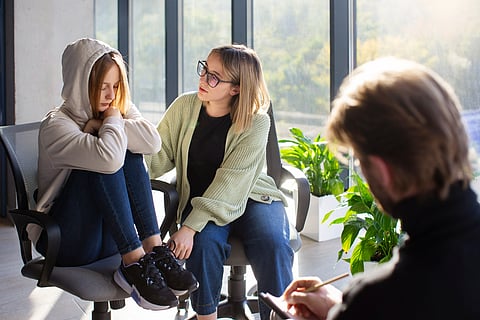 Teen girl and mom at therapy with therapist taking notes.