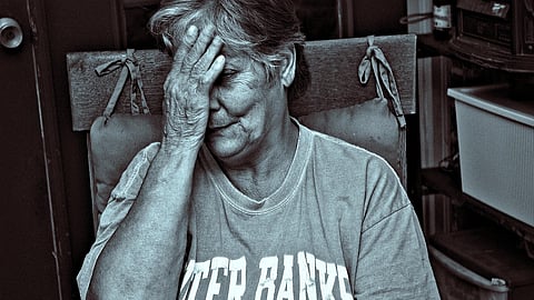 An elderly person sitting in  a chair with their hand covering part of their face.