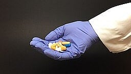 A Doctor's gloved hand holding multiple pills.