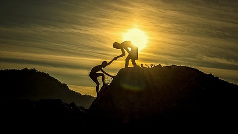 Picture shows one person helping the other climb up a foothill.