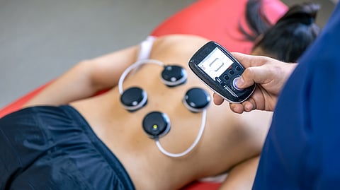 A woman using nerve stimulating devoice on her back with a remote.