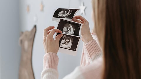 It shows a woman holding ultrasound images of her unborn baby, likely in a nursery.