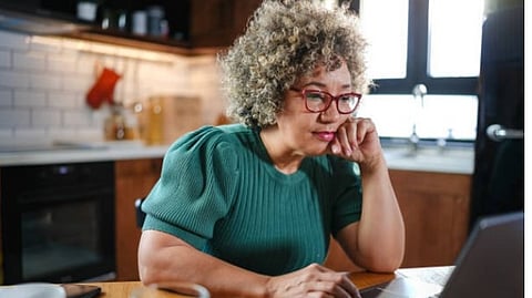 A woman wearing a green top with grey hair is reading something from a laptop.