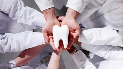 Multiple people wearing white coat placing their hands together to hold a tooth model.