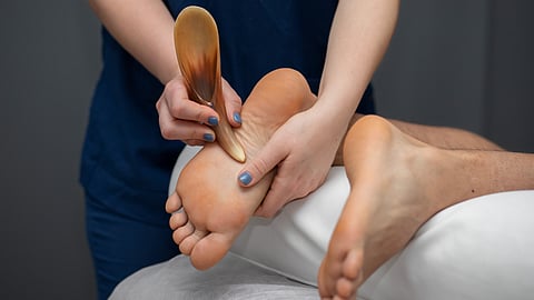 A person getting her feet massaged by a wooden Gua-sha tool by a podiatrist.