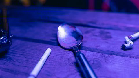 A dirty steel spoon and a roll on a wooden table indicating drug use.