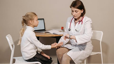 A girl child is getting a physical exam from a doctor who is checking the girl's pulse.