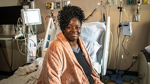 An image of Page Campbell in an orange robe sitting on a hospital bed.