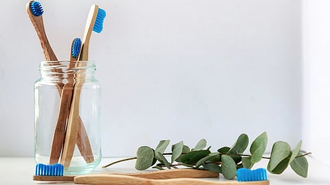 A glass jar holding bamboo toothbrushes with blue bristles