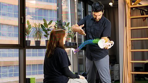 A person with a scoliosis vertebra model explaining something to another person.