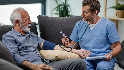 Happy general practitioner measuring blood pressure of mature man while being in a home visit
