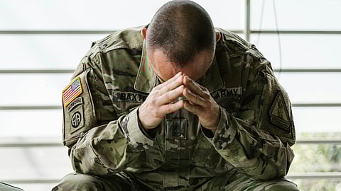 An US soldier wearing combats is sitting with his head bent down in his hands.