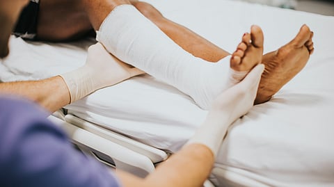 A leg is dressed from sole up to knee in gauze and a pair of hands are helping it onto a bed.
