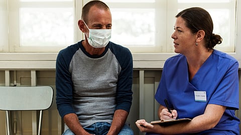 A female doctor is asking a male patient his symptoms for recording.