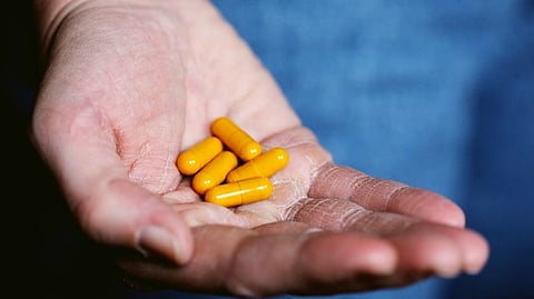 Five yellow capsules placed in the palm of a hand.