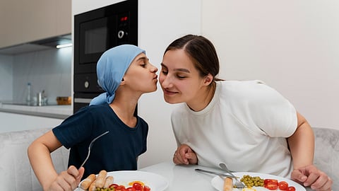 A child gives a kiss on the cheek of his mother and eats a healthy breakfast.