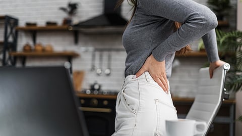 A woman clutching her back while standing up from a chair.