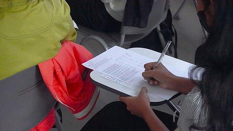 A woman seated in a chair, writing on paper with a pen in her hand.