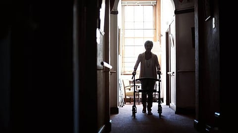 A silhouette of a person using a walker, navigating a dimly lit corridor.