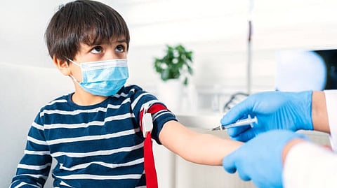 A child sits while a healthcare professional collects blood with a syringe in a clinic.