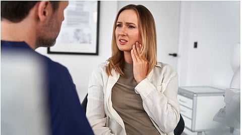 A lady holding her hand on her cheek indicating tooth ache in a clinic.