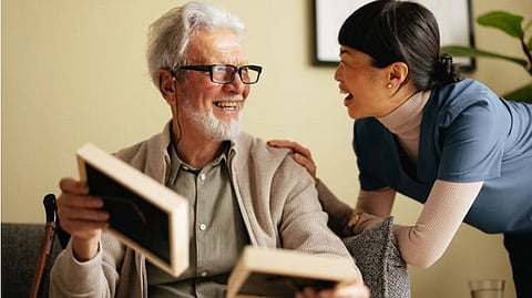 An elderly man is talking to a young nurse; both are smiling.