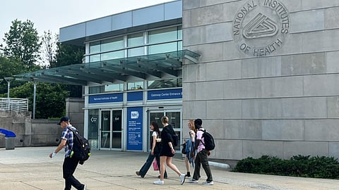 An image of a grey building with few people walking in front of them.