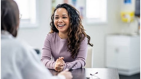 A woman smiling at another person sitting at a table across her in between a conversation.