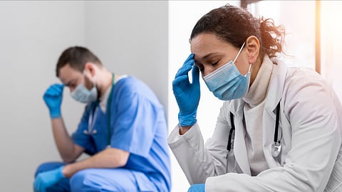 Two healthcare workers, one male and female sitting on the floor looking tired and distressed.