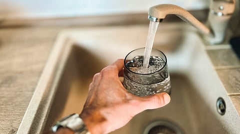 A person holding a glass of water in front of a kitchen sink, ready to drink.