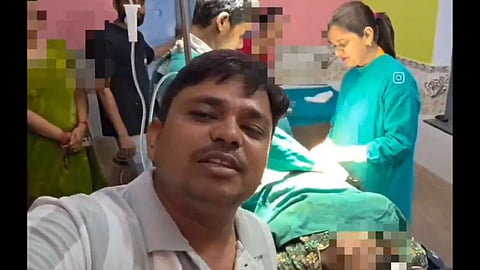 A man and a woman smile for a selfie in a hospital setting, with medical equipment visible in the background.