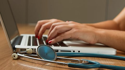 A person using a laptop and a stethoscope nearby.