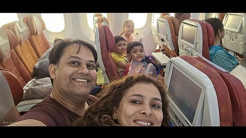 A selfie of parents with their three children, all smiling, looking at the camera and sitting inside plane.