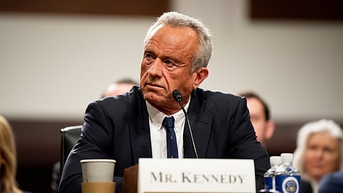 An image of Kennedy sitting at a table in front of a mike at a hearing.