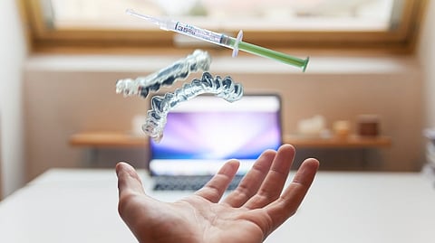 A hand catches a floating syringe and dental aligners above an open laptop.