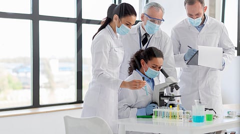 A group of people in lab coats examining a sample in a pharmaceutical company laboratory setting.