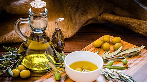 Glass olive oil bottle and a bowl of olive oil, accompanied by fresh olives and green leaves.