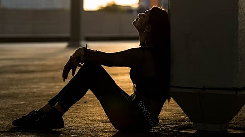 A woman sitting on concrete pavement in a dark alley.