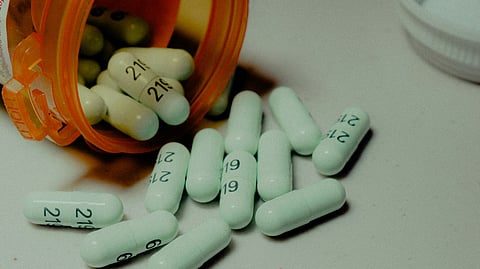 A clear bottle filled with various colored pills, labeled with dosage instructions and a childproof cap.