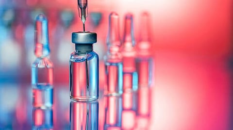 A close-up of a glass vial with a needle poised above it, surrounded by blurred ampoules.
