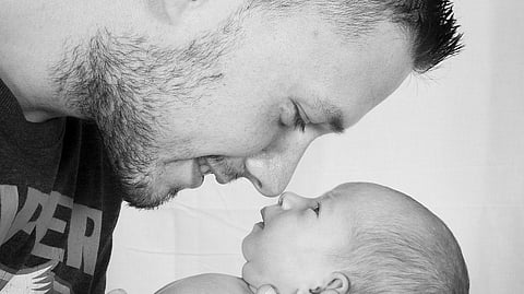 A father affectionately touches noses with his newborn baby, cradled in his arms. 