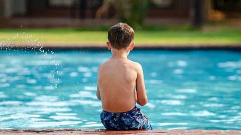 A young boy sitting on the edge of a swimming pool.